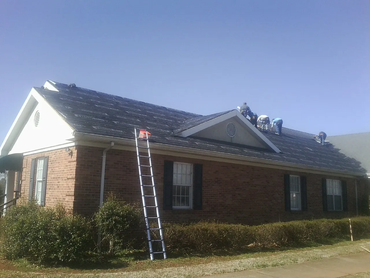 Crew tearing shingles off a brick ranch roof with a ladder set — Emergency Roof Repair work by our crew in Lake Butler