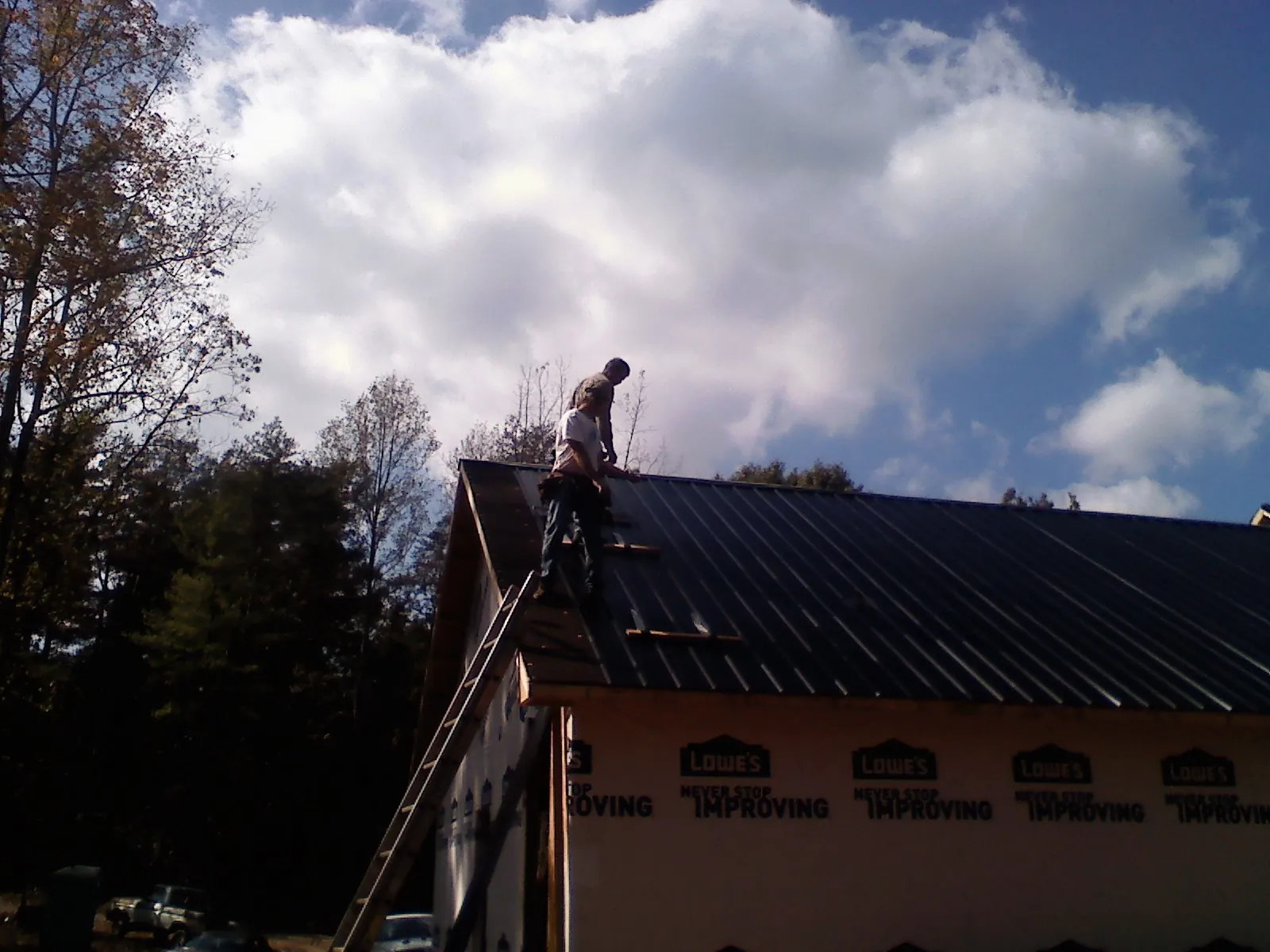 Roofer fastening dark metal panels high against a cloudy sky, from a Roof Inspection job in Lake Butler