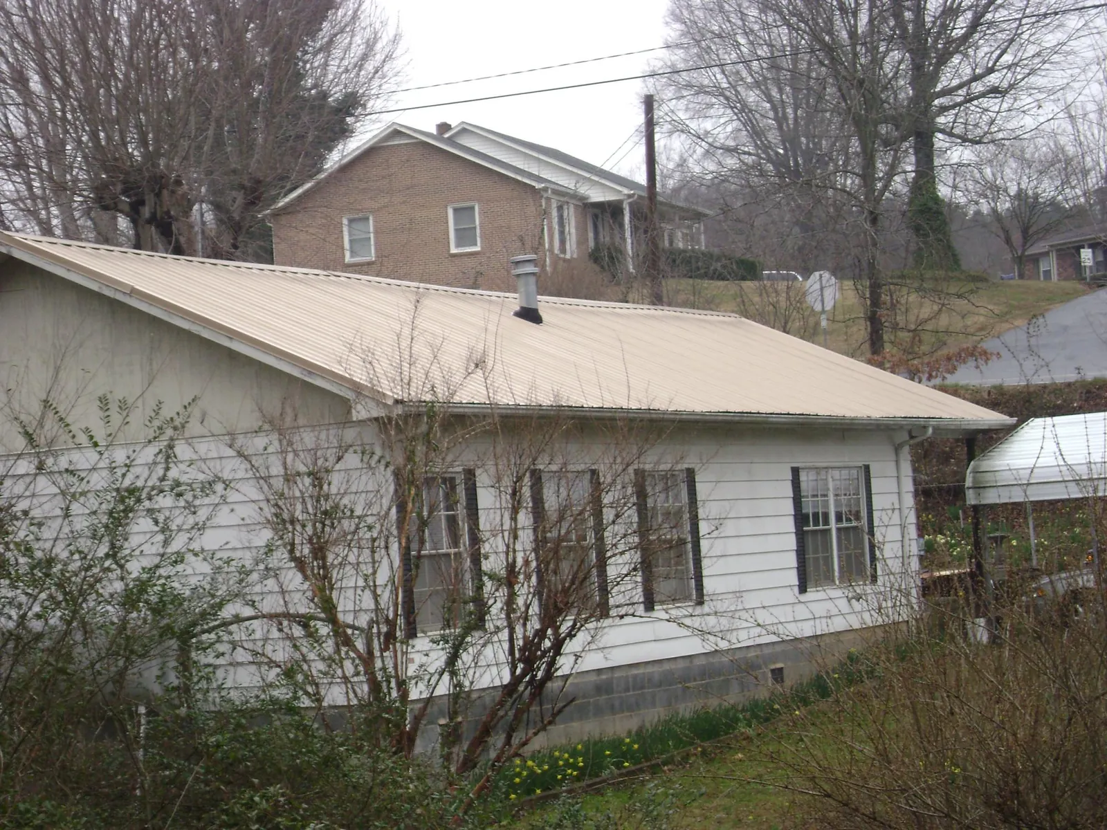 Tan metal roof on a white sided house set into a hillside — Commercial Roofing by Roofing Brothers in Lake Butler